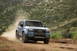 2027 Toyota Land Cruiser driving on dirt trail kicking up dust in an off-road rugged terrain