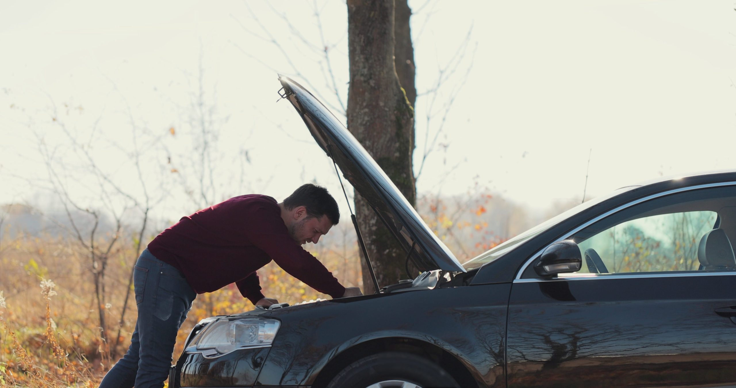 Man trying to fix his broken down car on the side of the road